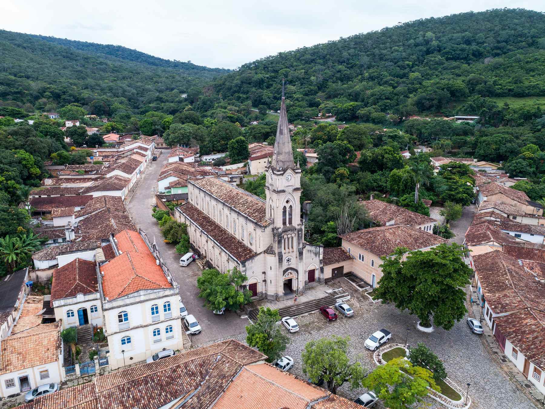 Vista aérea do centro histórico da Cidade de Goiás, com a Igreja do Rosário de torre pontiaguda no meio do casario de telhados de barro, ruas de pedra e os morros verdes em volta.