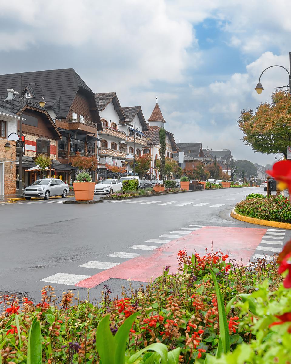 Rua do centro de Gramado num dia frio e nublado de outono, com canteiro de flores vermelhas em primeiro plano.