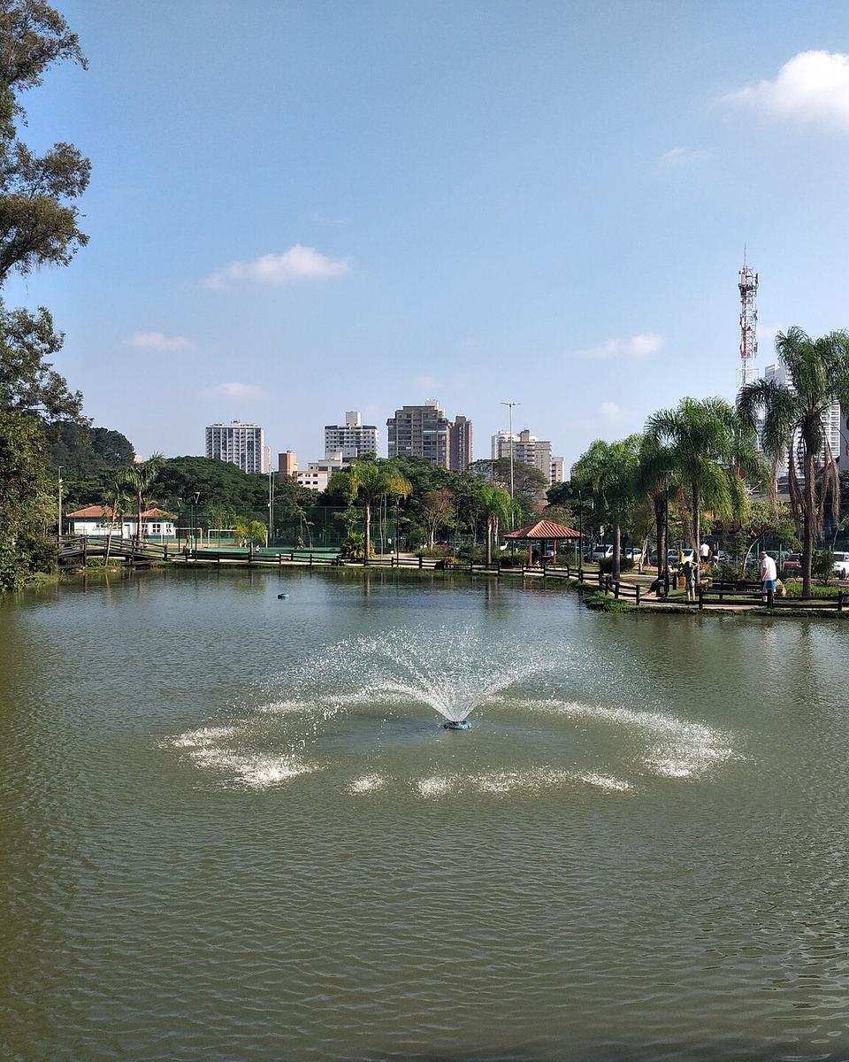 Lago central do Bosque Maia, em Guarulhos, com chafariz e prédios ao fundo.
