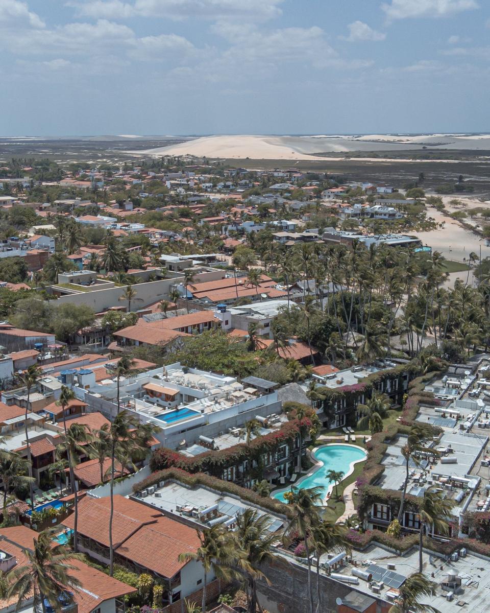 Vista aérea da vila de Jericoacoara, com pousadas entre coqueiros e as dunas ao fundo.