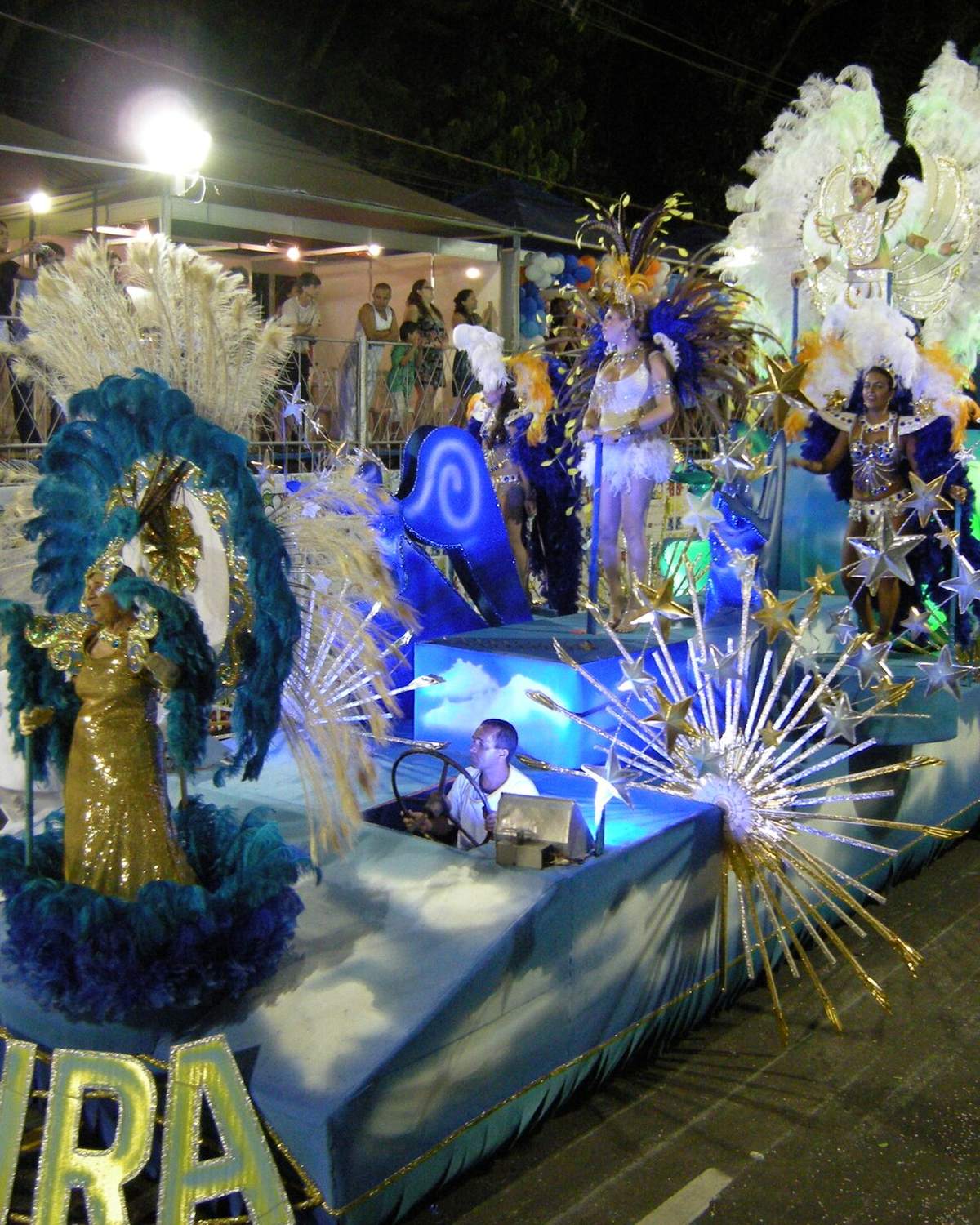 Carro alegórico com destaques de plumas desfilando à noite no carnaval de Juiz de Fora.