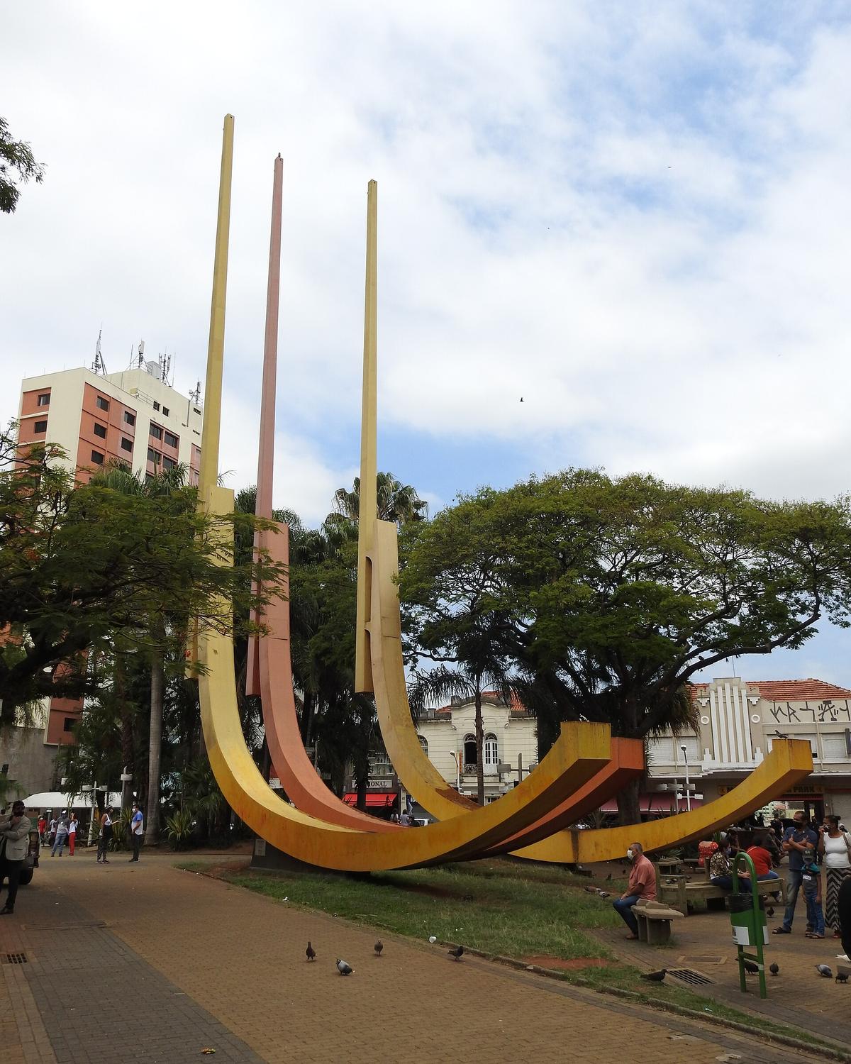 Praça no Centro de Jundiaí com pessoas nos bancos e a escultura Esquadra.