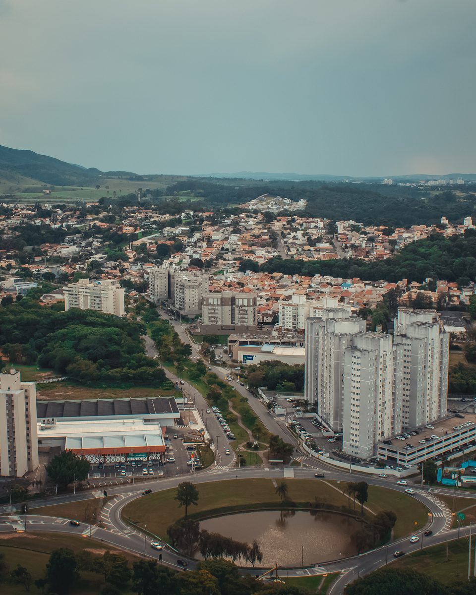 Vista aérea de Jundiaí com prédios, casas e avenidas arborizadas, um lago numa rotatória em primeiro plano e a Serra do Japi à esquerda, no horizonte.