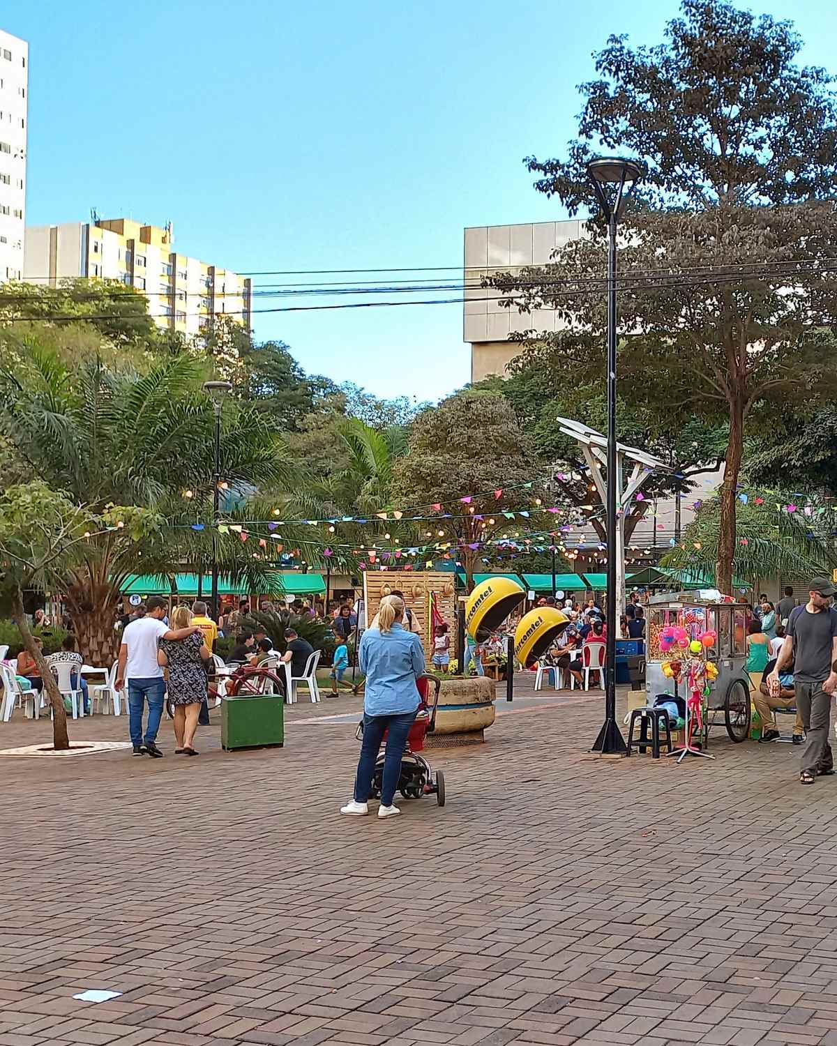 Moradores passeando pelo Calçadão de Londrina num fim de tarde, com mesas de lanchonete, bandeirinhas coloridas, carrinhos de pipoca e prédios do Centro ao fundo.
