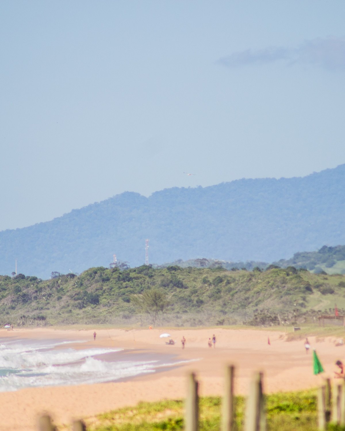 Banhistas na areia da Praia do Pecado, em Macaé, com a serra ao fundo.