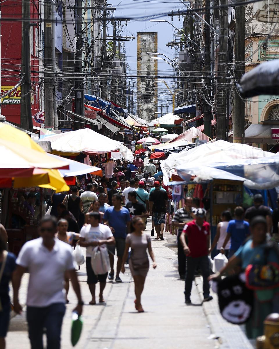 Rua de comércio popular no centro de Manaus, cheia de pedestres, barracas de camelô e toldos de lona nos dois lados.
