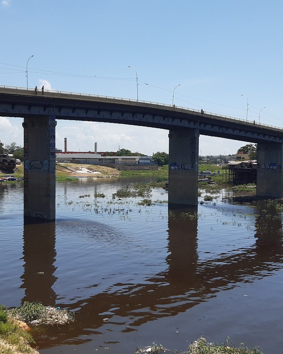 Ponte do Educandos sobre o igarapé, em Manaus, com palafitas de madeira e barcos encostados na margem.