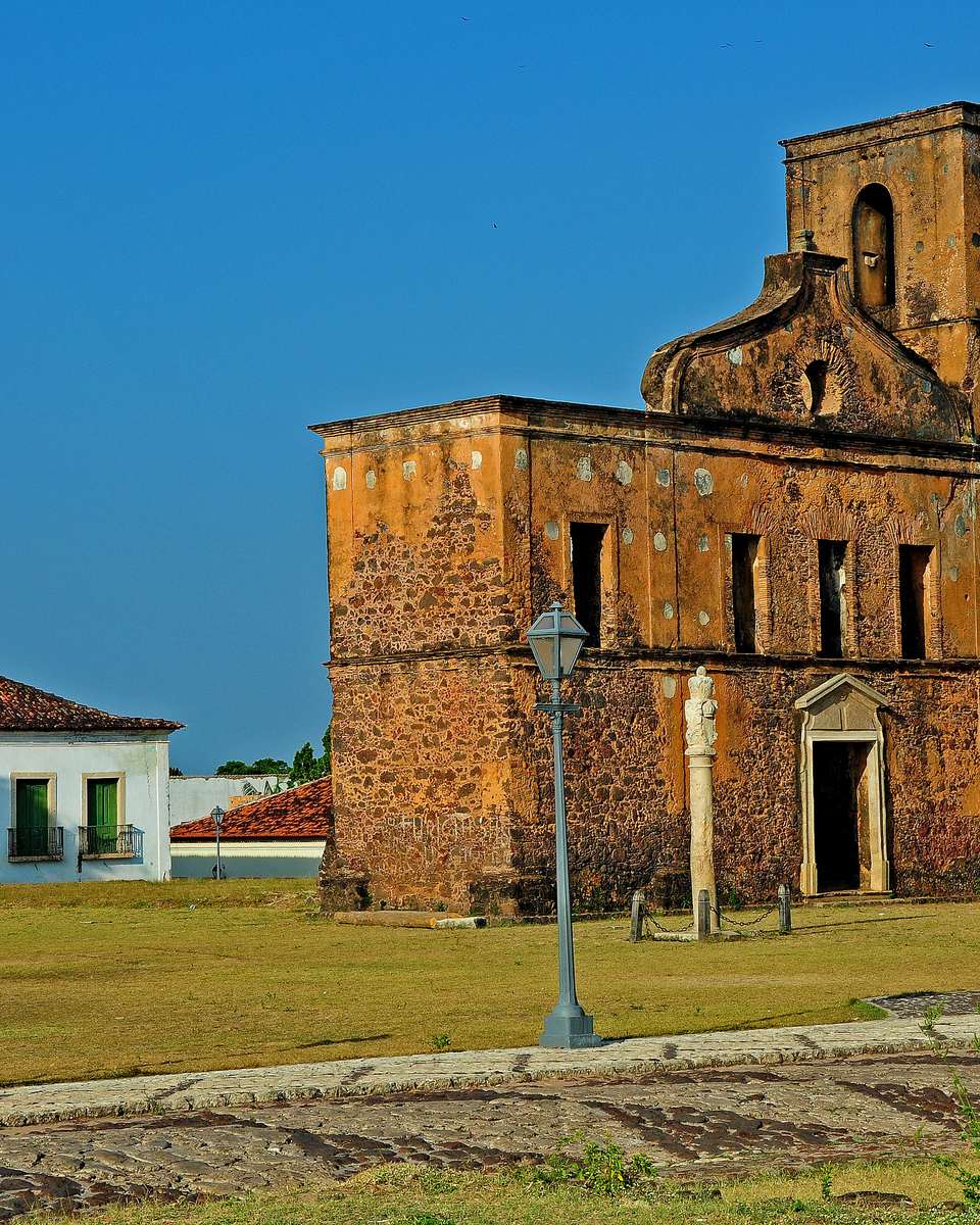 Ruínas de pedra da Igreja de São Matias na praça de Alcântara, com o pelourinho ao lado e casario colonial branco ao fundo