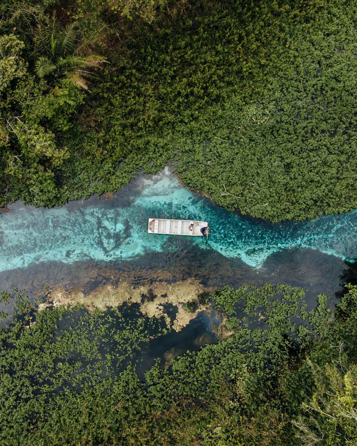 Vista de drone do rio de água azul-turquesa em Bonito, com um barco de flutuação parado no meio do rio e mata fechada nas duas margens.