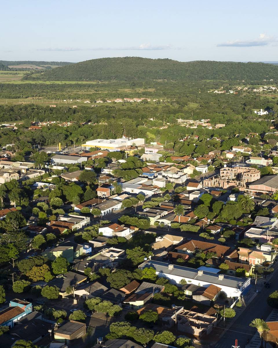 Vista aérea da cidade de Bonito, com ruas arborizadas, casas de telhado vermelho e a serra ao fundo em dia de sol.