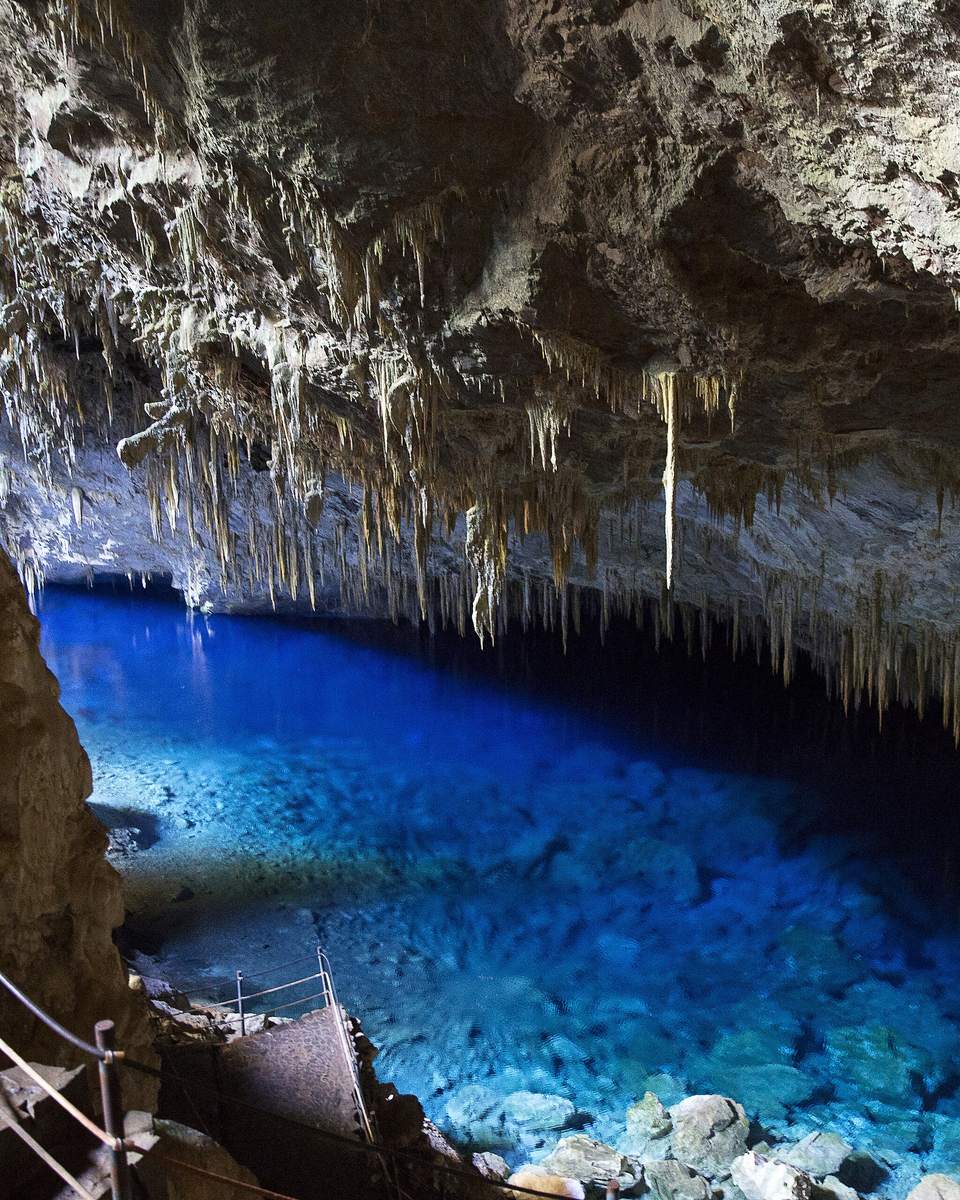 Interior da Gruta do Lago Azul, em Bonito, com estalactites no teto da caverna e o lago de água azul-cobalto no fundo.