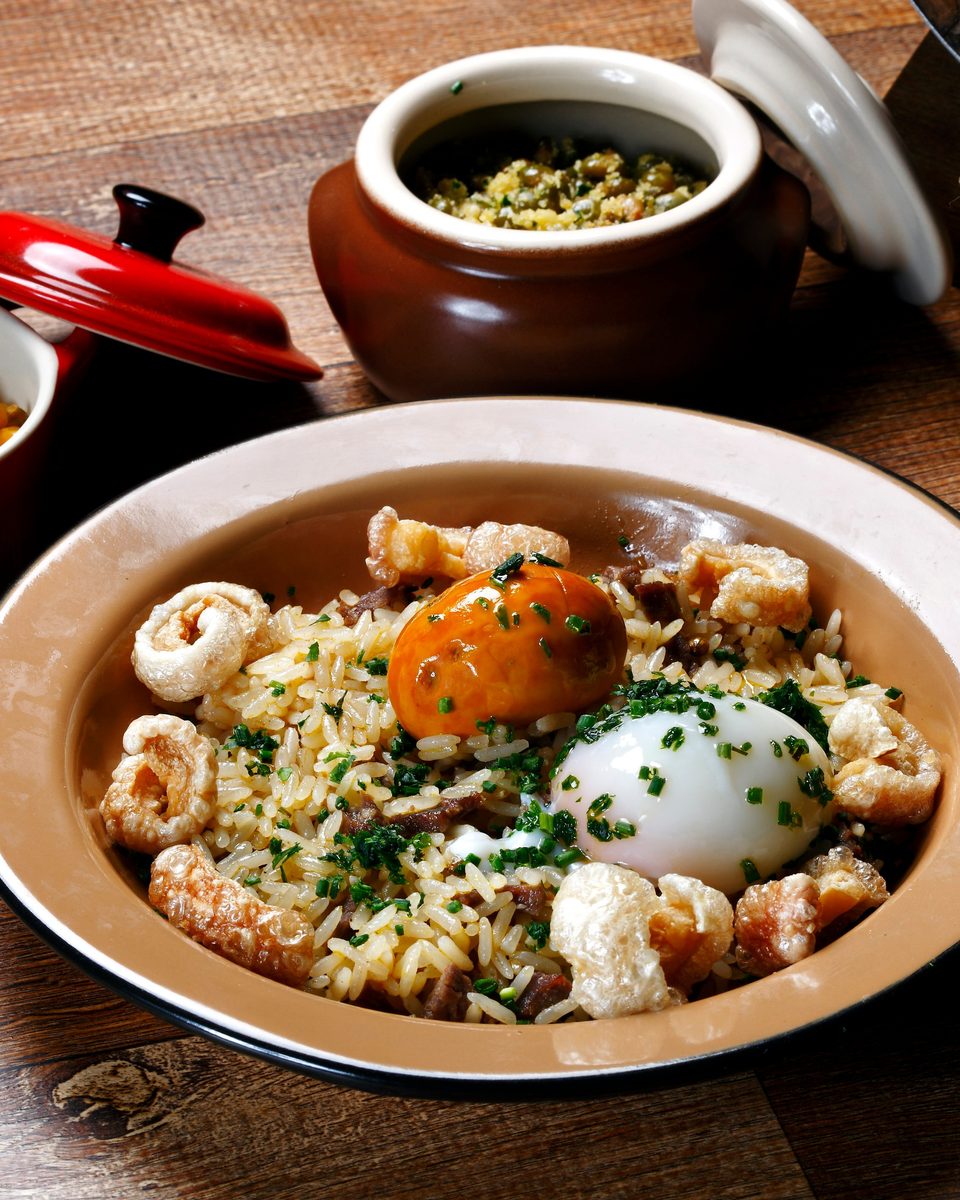 Prato de arroz com pequi, torresmo e ovo, com pimenta e uma dose de cachaça ao lado.