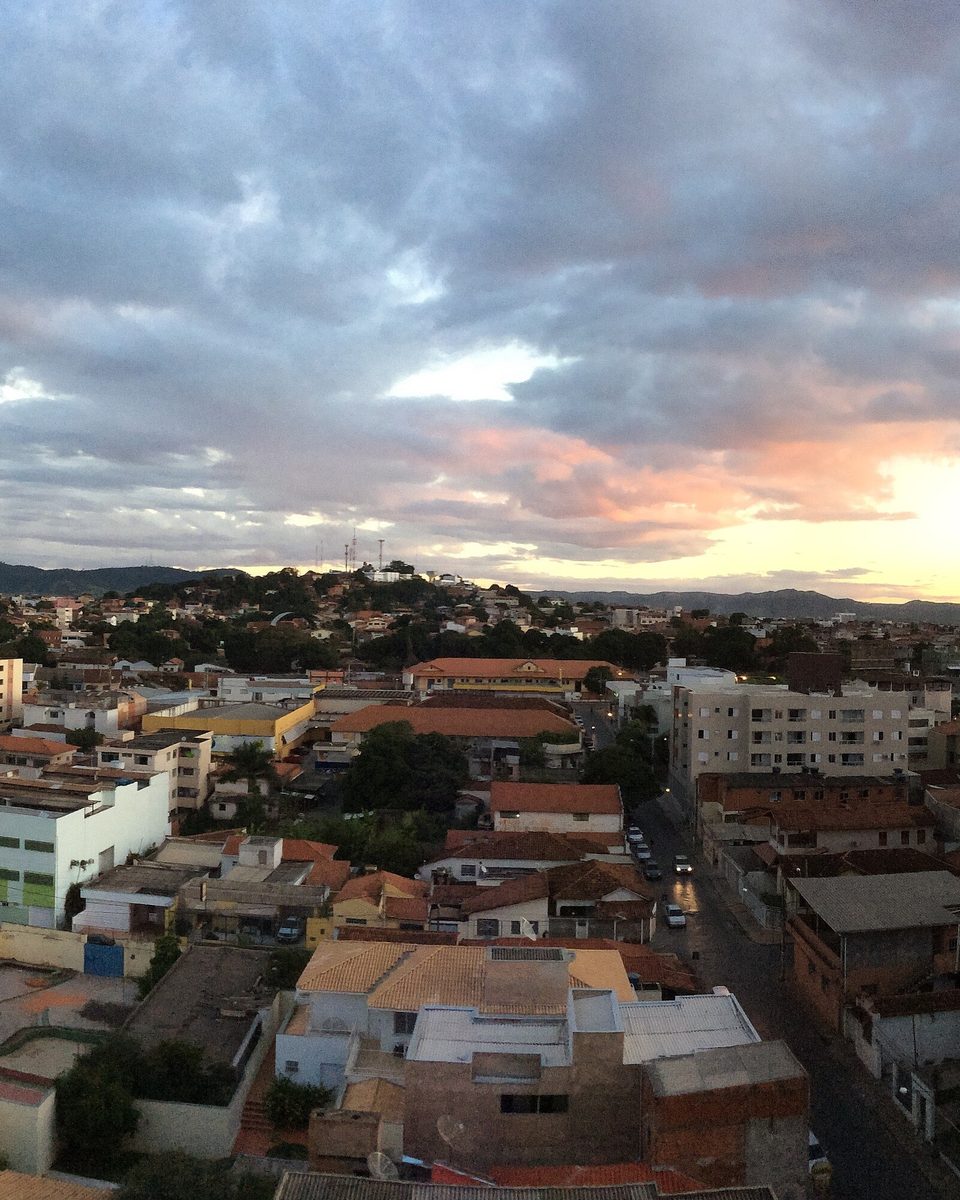 Vista do alto de Montes Claros ao entardecer, com casas, prédios e a serra ao fundo.