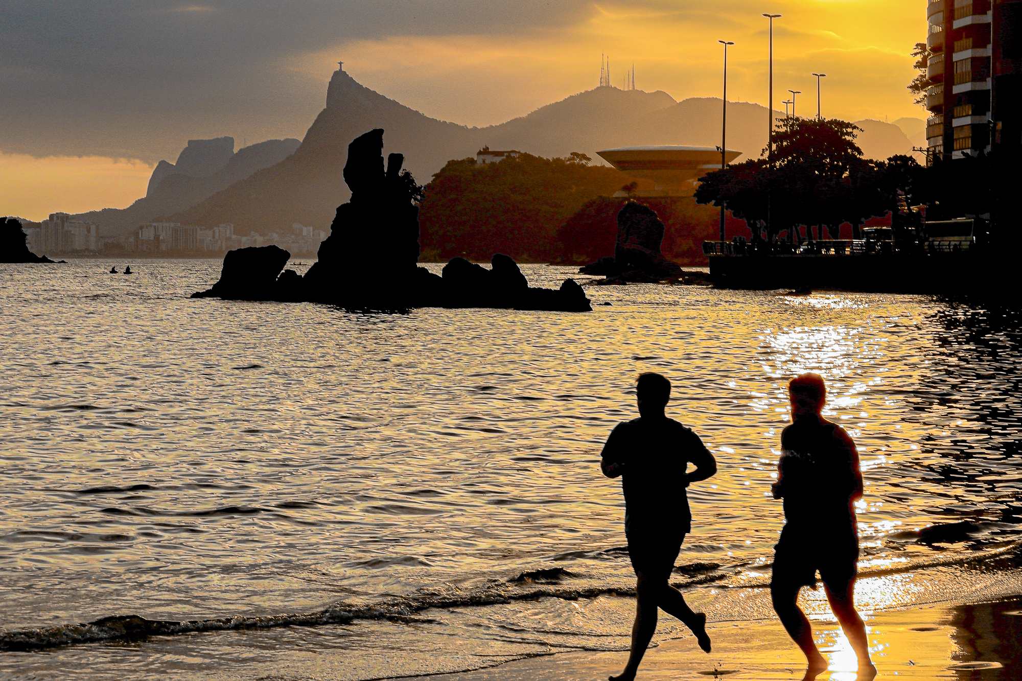 Pessoas correndo na Praia de Icaraí, em Niterói, ao pôr do sol.