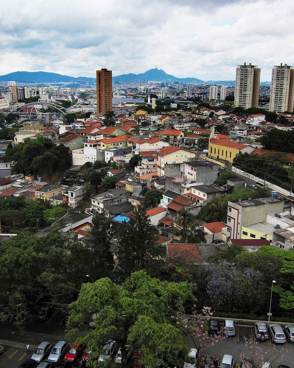 Vista do alto de Osasco, com casas, prédios e árvores até o horizonte e montanhas ao fundo.