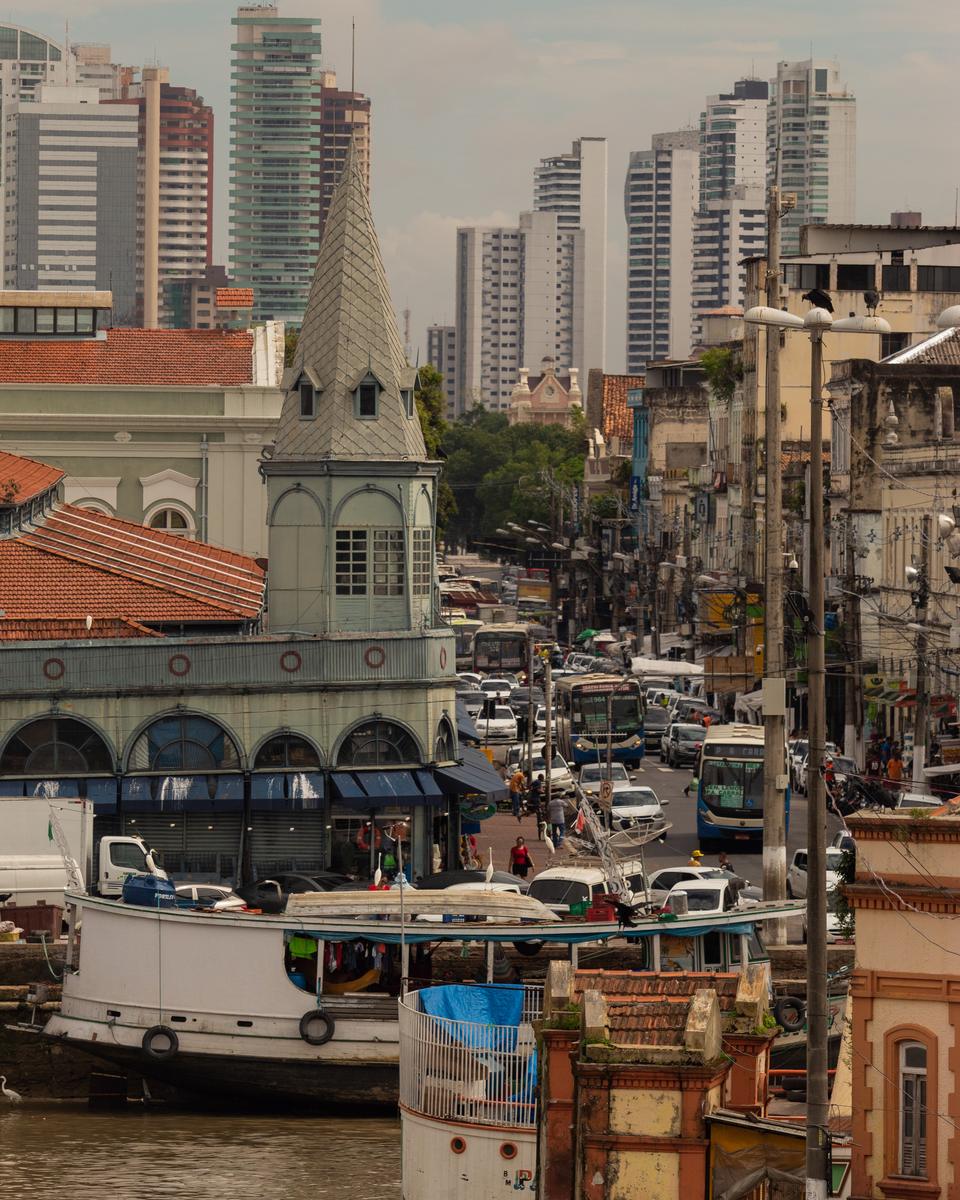 Torre do mercado do Ver-o-Peso em primeiro plano e, atrás, a rua do centro de Belém com ônibus, carros e comércio.