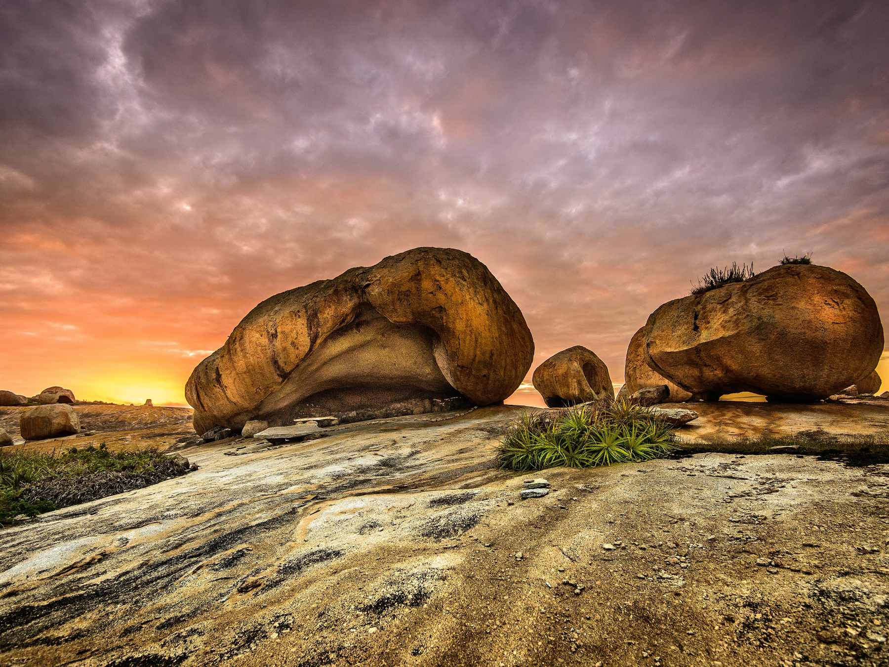 Blocos arredondados de granito do Lajedo de Pai Mateus, em Cabaceiras, apoiados sobre a laje de pedra ao amanhecer, com o céu alaranjado no horizonte
