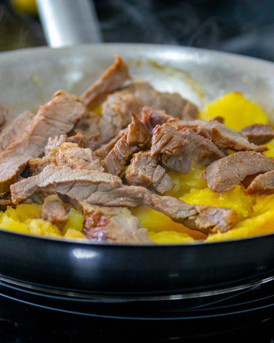 Carne de sol desfiada servida sobre pedaços de macaxeira cozida em uma frigideira quente