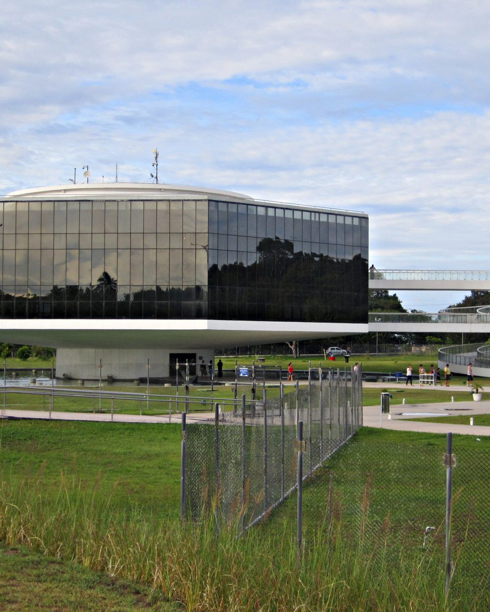 Prédio de vidro da Estação Cabo Branco, projetada por Oscar Niemeyer, com a torre-mirante em rampa e visitantes caminhando pelo entorno
