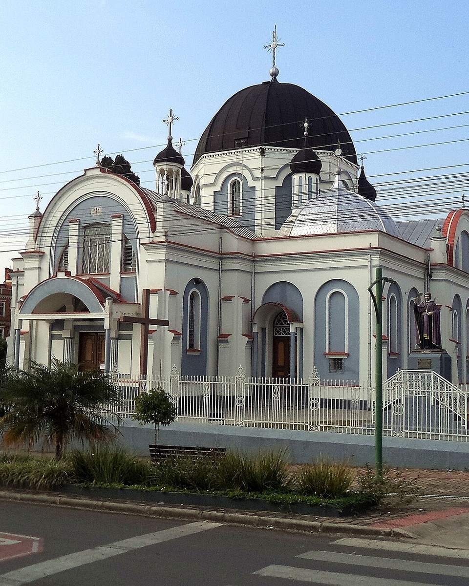 Igreja ucraniana de São Josafat, em Prudentópolis, com fachada branca e azul, cúpula escura, torres com cruzes e gradil branco, vista da esquina num fim de tarde.