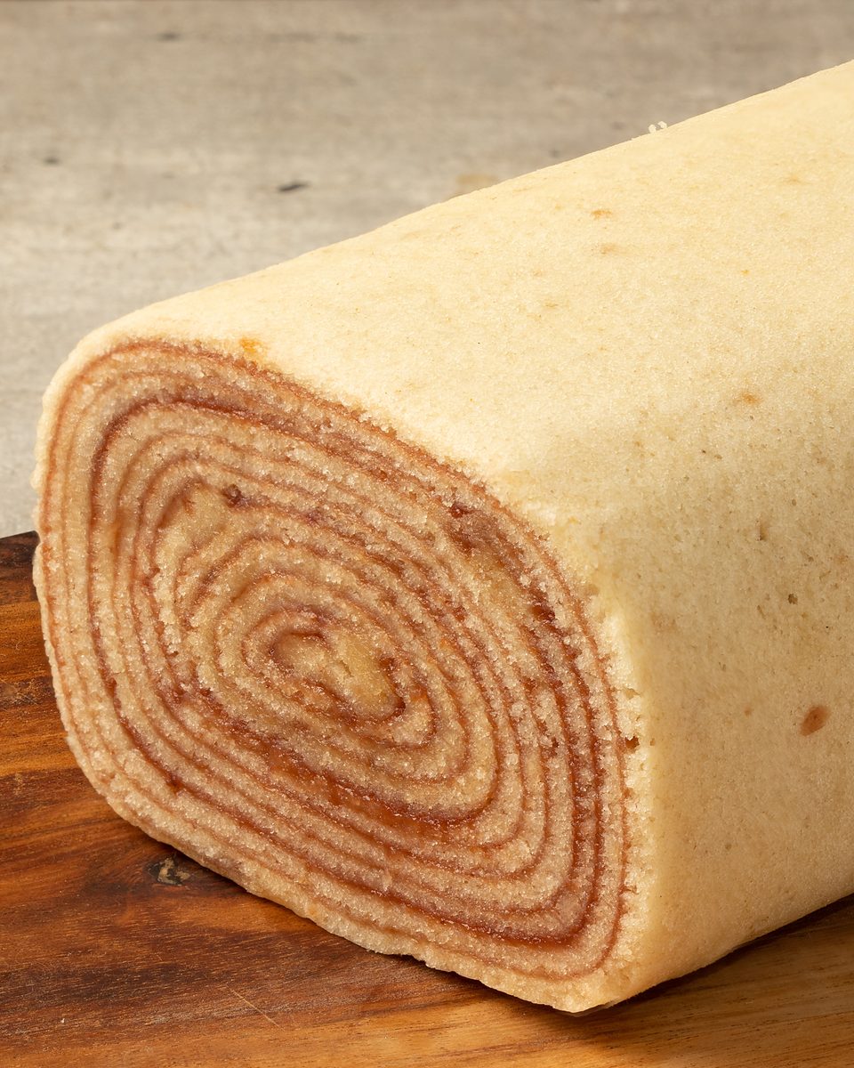 Bolo de rolo cortado sobre uma tábua de madeira, mostrando as camadas finas enroladas em espiral com recheio de goiabada.