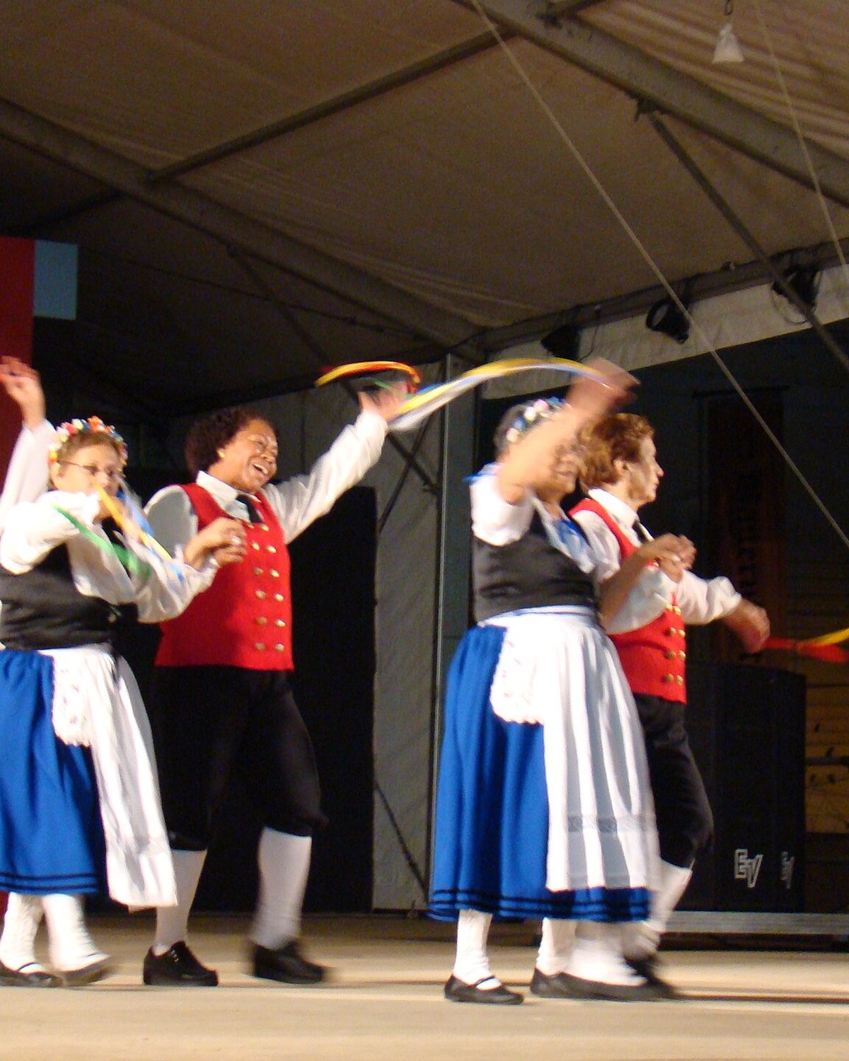 Mulheres com trajes típicos alemães dançando com fitas coloridas no palco da Bauernfest, em Petrópolis.