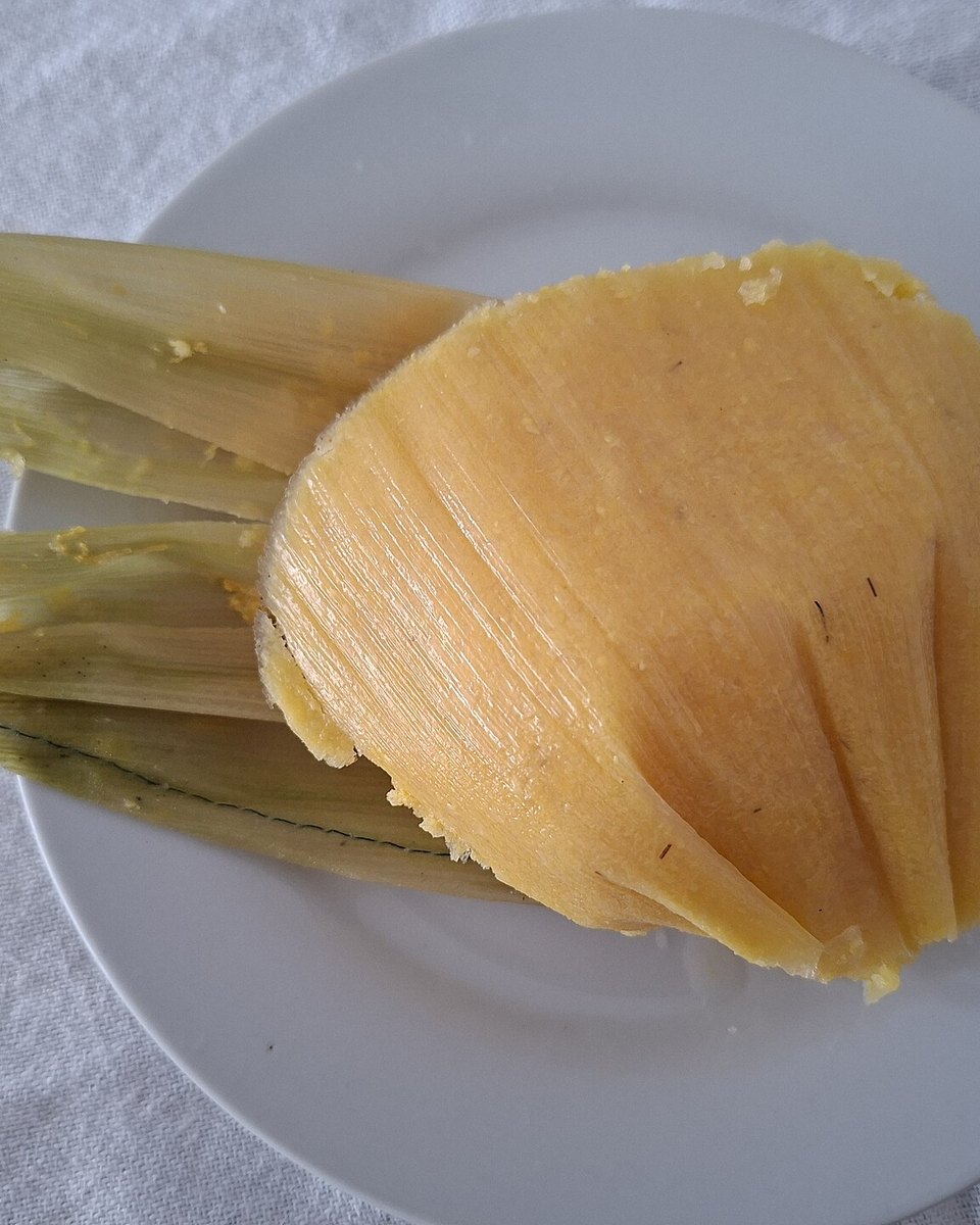 Pamonha de Piracicaba servida num prato branco, aberta ao lado da palha verde do milho.