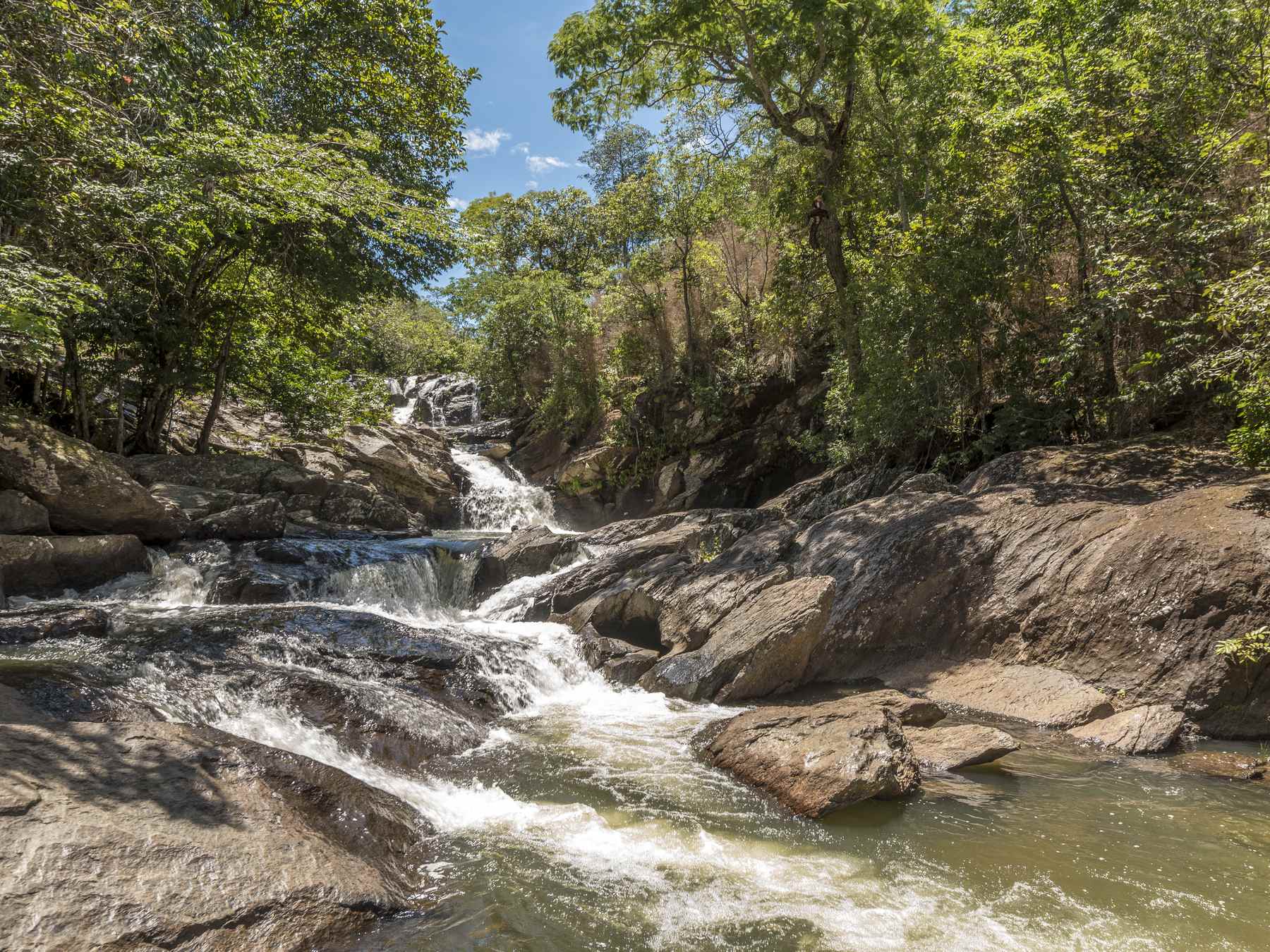 Corredeiras da Cachoeira Meia Lua, em Pirenópolis, com a água branca correndo entre grandes pedras arredondadas e a mata do cerrado nas margens.