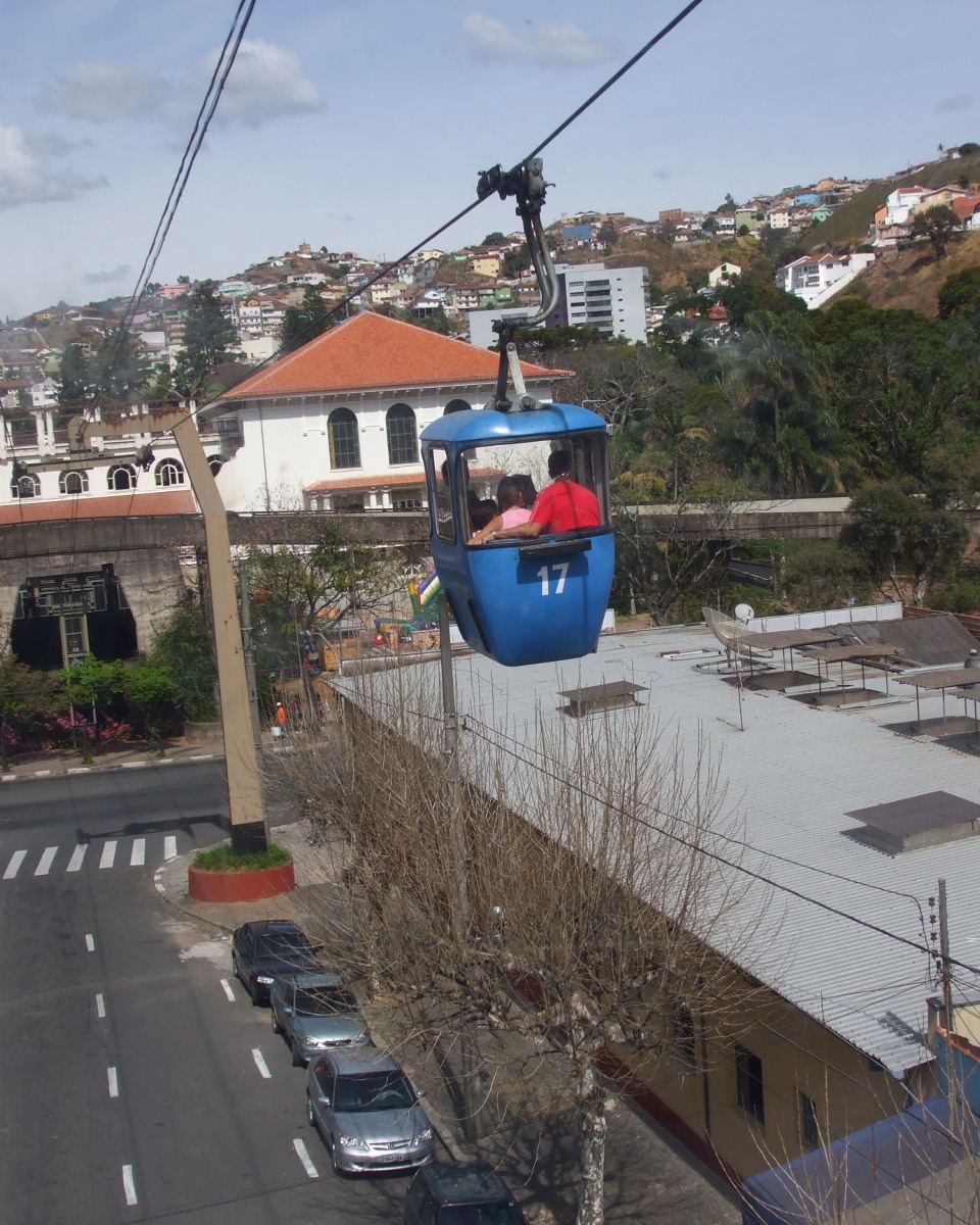 Cabine azul do teleférico de Poços de Caldas passando sobre o centro da cidade, com o casario e a serra ao fundo.