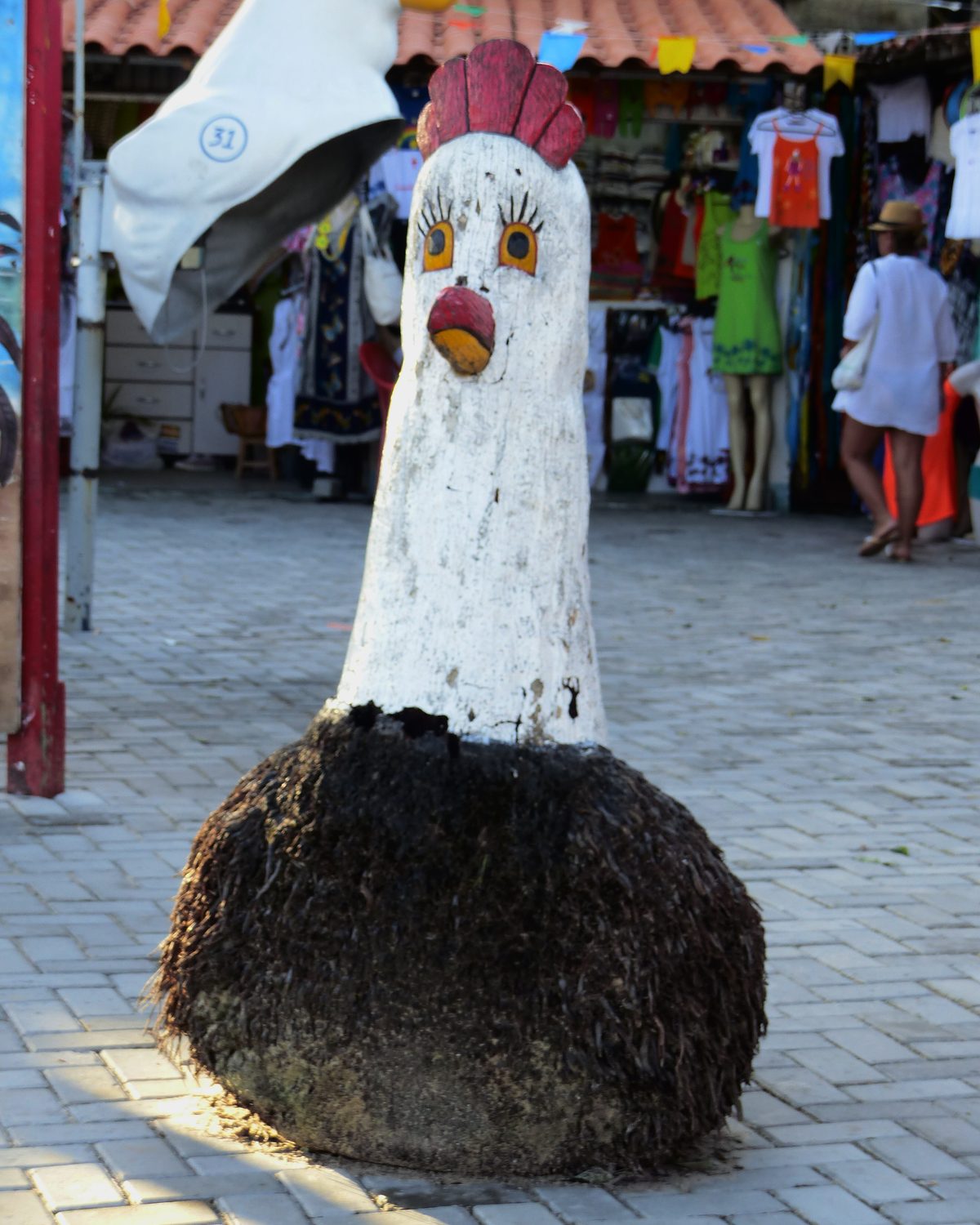 Escultura de galinha de madeira numa calçada da vila de Porto de Galinhas.