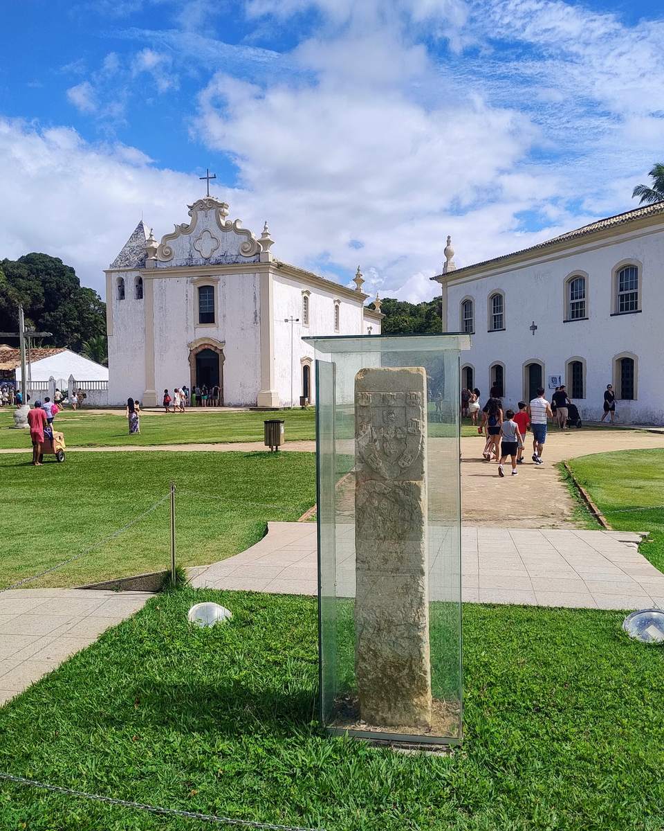 Cidade Alta de Porto Seguro com a igreja e o casario brancos e o Marco do Descobrimento no gramado.