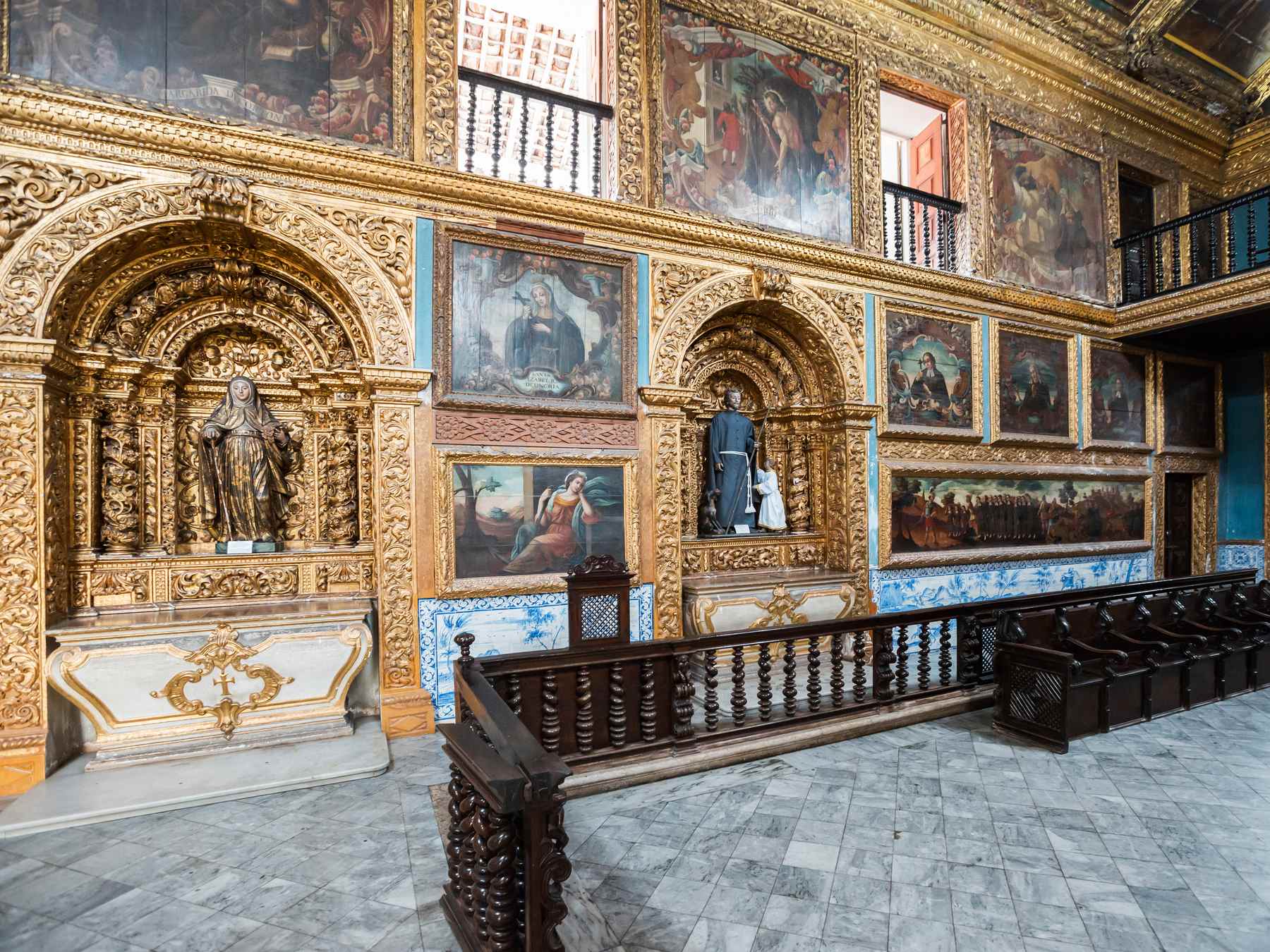 Interior da Capela Dourada, no bairro de Santo Antônio, com altares de talha dourada, painéis de pintura nas paredes, azulejos azuis e bancos de madeira escura sobre o piso de pedra.