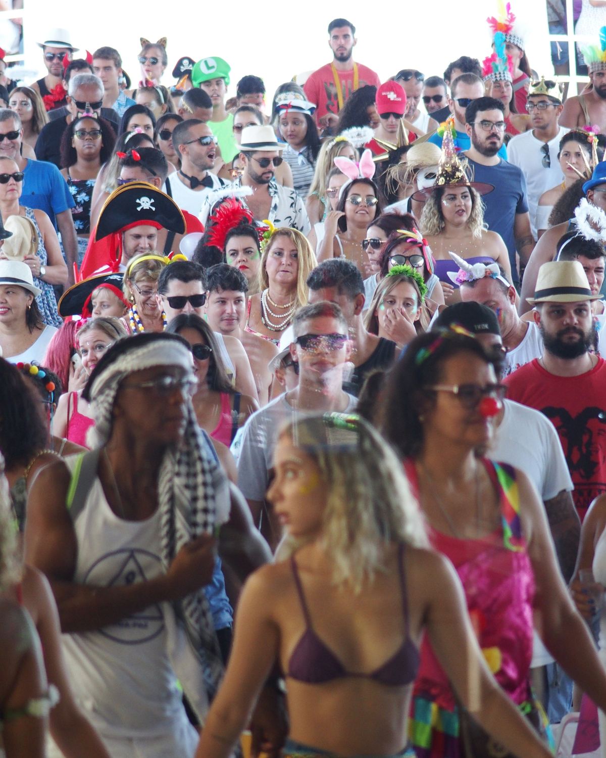 Multidão de foliões fantasiados, com chapéus, óculos e adereços coloridos, na chegada da barca de Niterói no Carnaval.