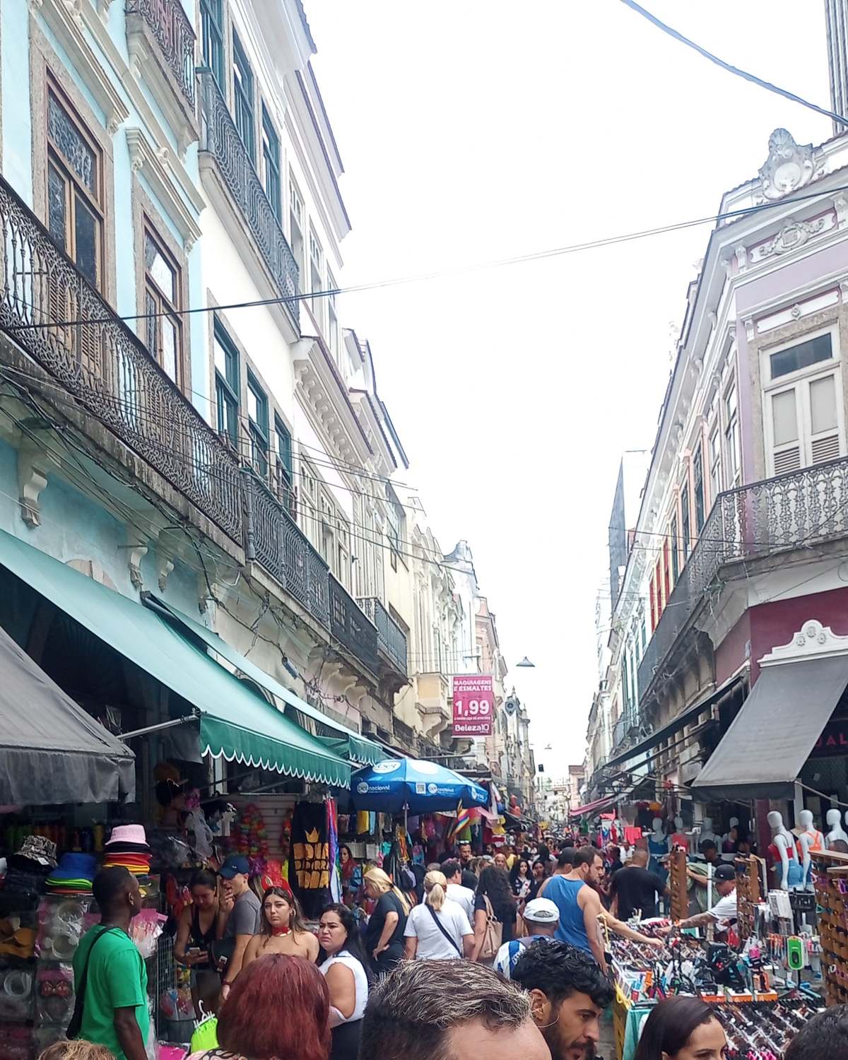 Rua estreita do Saara, no Centro do Rio, cheia de gente entre lojas de chapéus, fantasias e acessórios, com sobrados antigos dos dois lados.