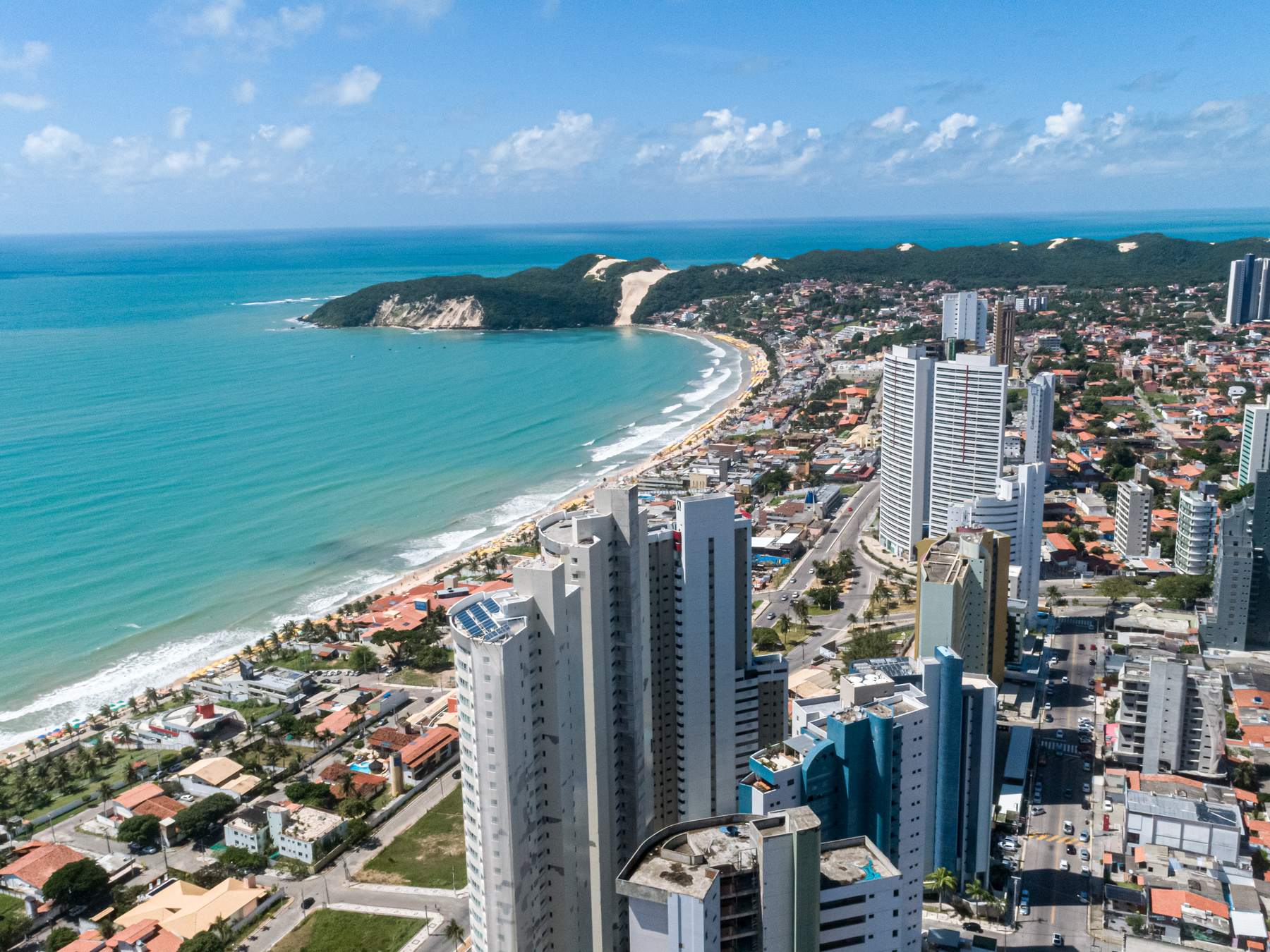 Vista aérea da praia de Ponta Negra em Natal, com a duna do Morro do Careca ao fundo e os prédios da orla à direita