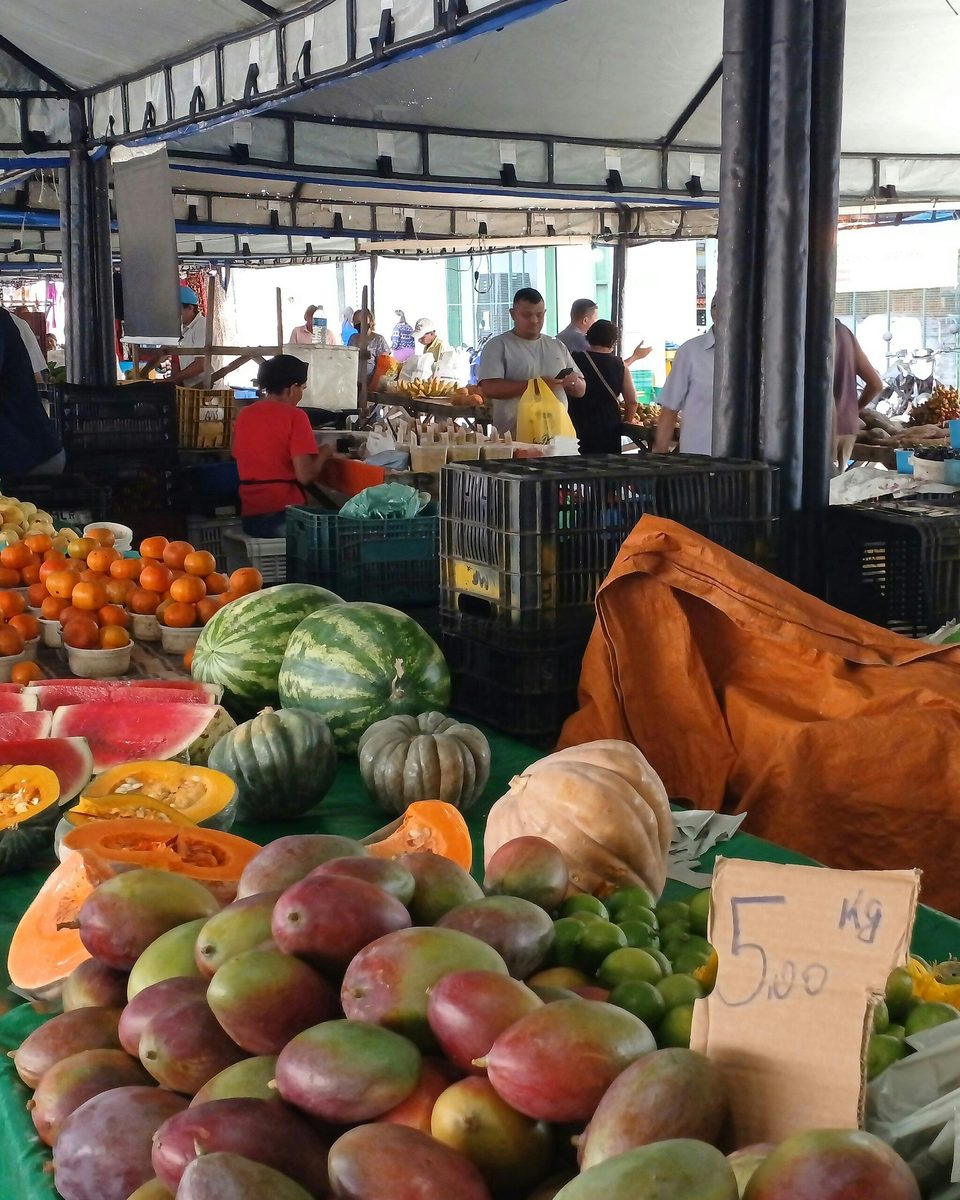 Bancas cobertas de frutas e verduras na feira do Alecrim, em Natal, com feirantes e clientes entre as mesas