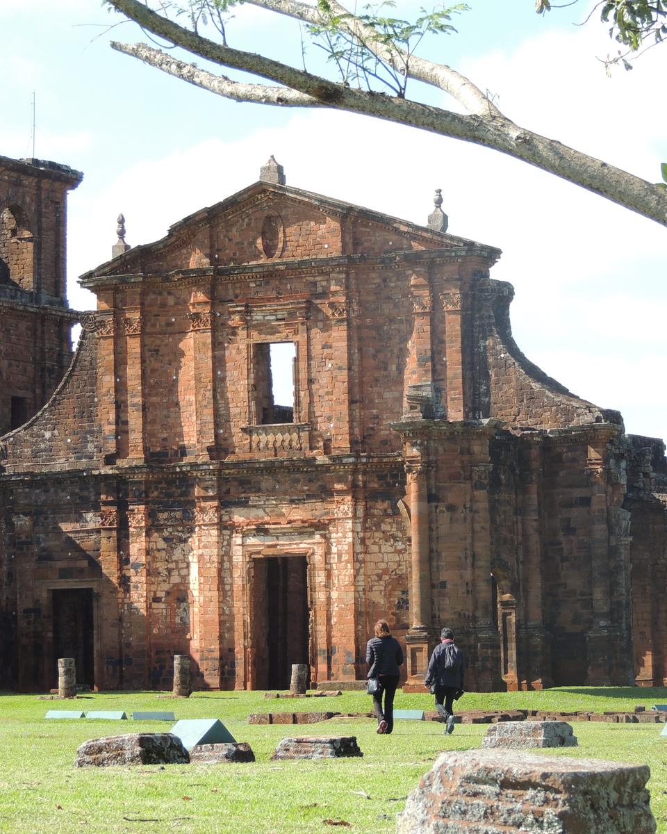Fachada de pedra das ruínas da igreja de São Miguel Arcanjo, com o gramado do sítio arqueológico e visitantes caminhando, em São Miguel das Missões.