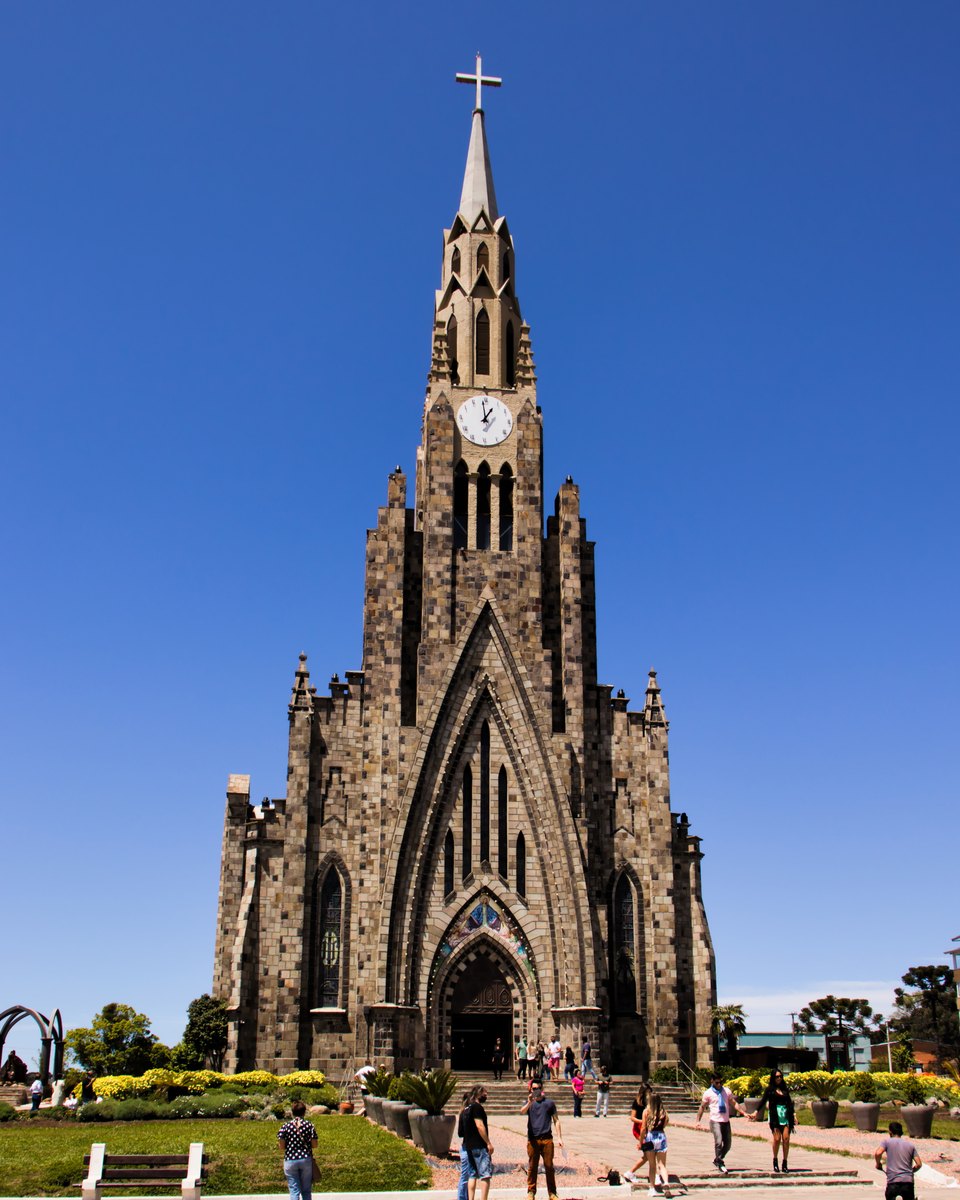 Catedral de Pedra de Canela, de estilo gótico e torre pontiaguda, com visitantes na praça em frente, sob céu azul.