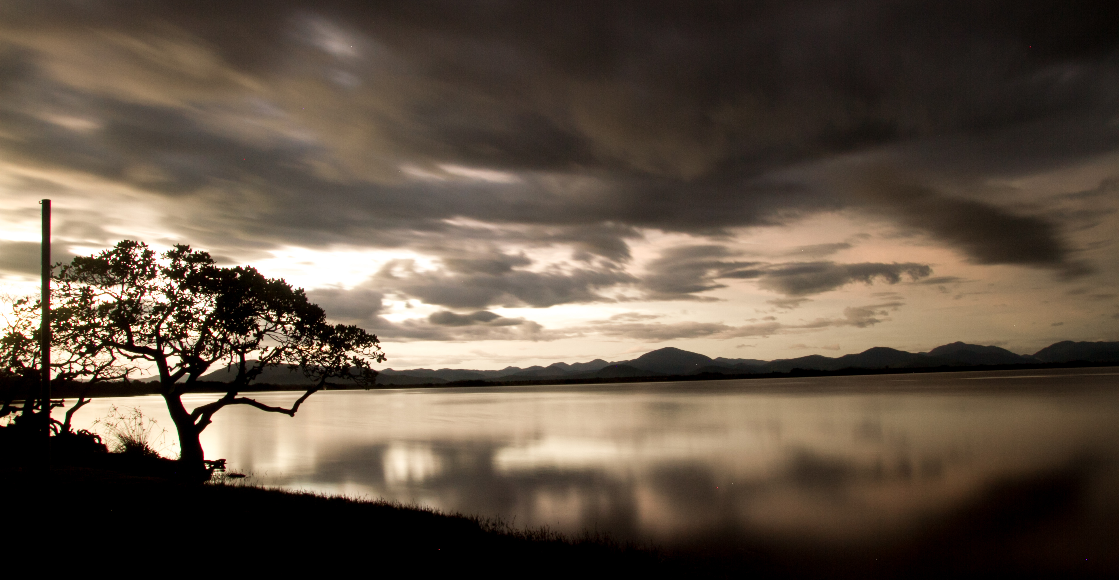 Lago Caracaranã ao entardecer, com as águas paradas refletindo o céu alaranjado e formações rochosas na margem