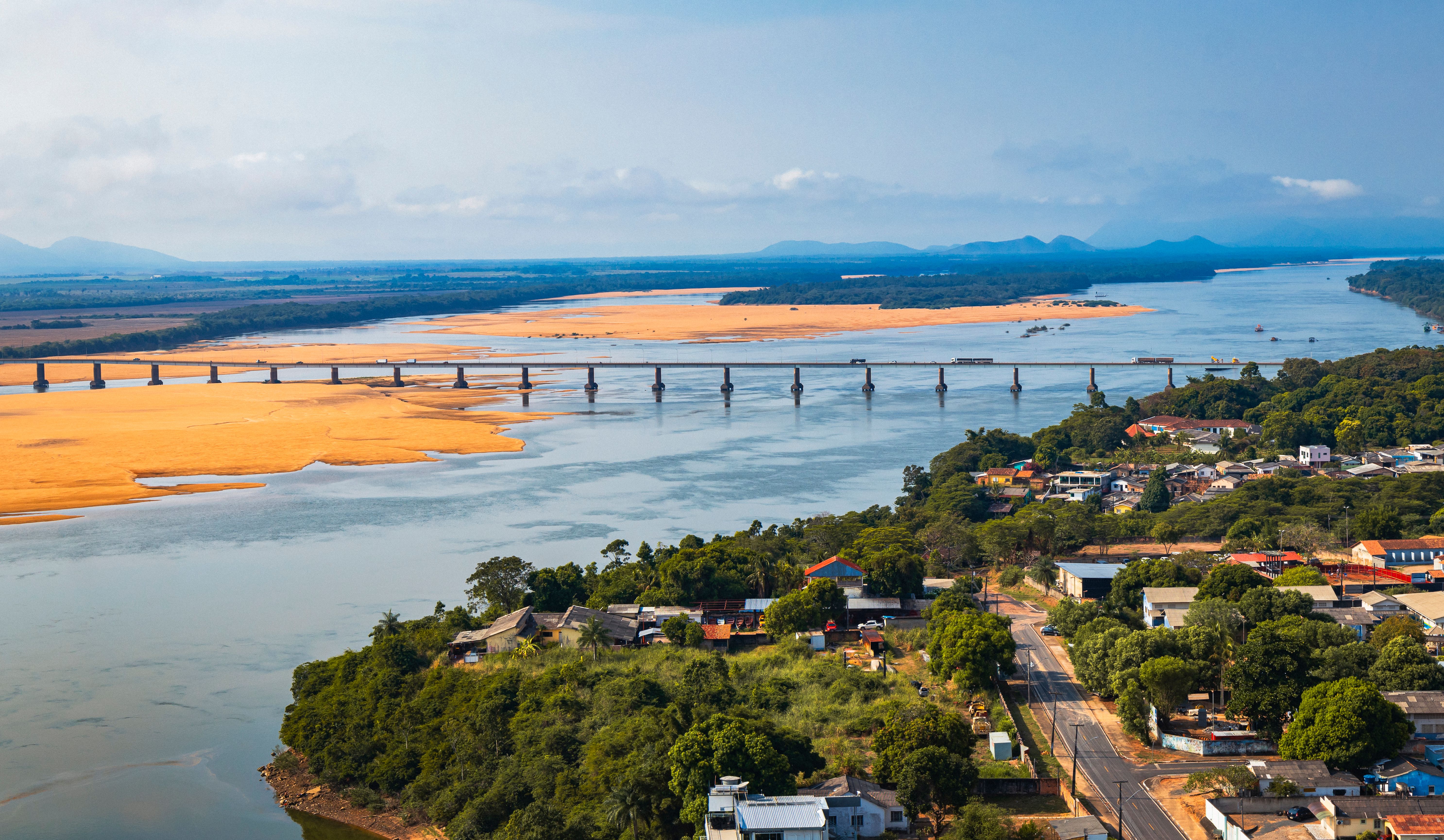 Vista aérea de uma ponte sobre um rio em Boa Vista, com vegetação densa nas margens e o traçado da cidade ao fundo