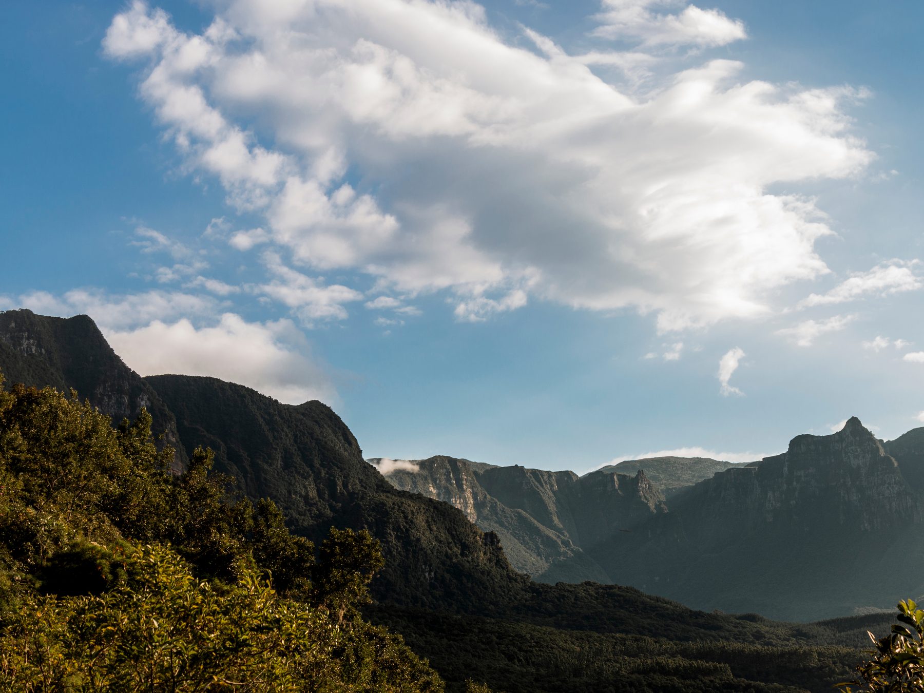 Paredões e picos da Serra do Corvo Branco cobertos de mata, sob um céu azul com nuvens brancas.