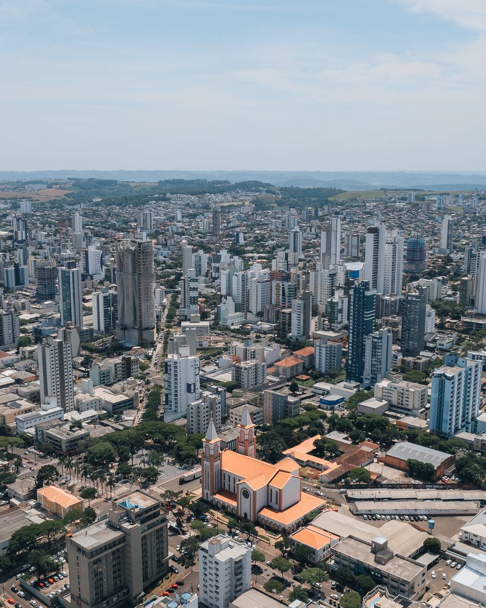 Vista aérea do centro de Chapecó, com prédios altos, avenidas largas e a Catedral Santo Antônio no meio da cidade.