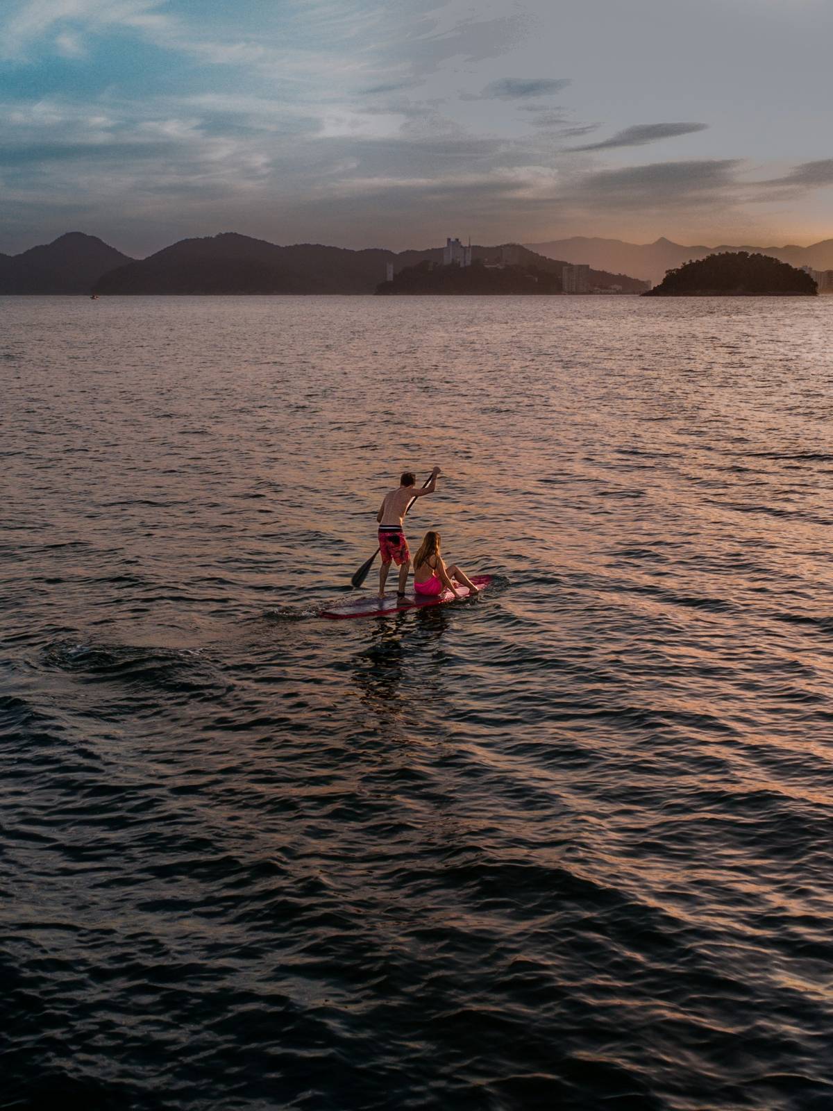 Duas pessoas remando de stand up paddle no mar de Santos, ao entardecer.