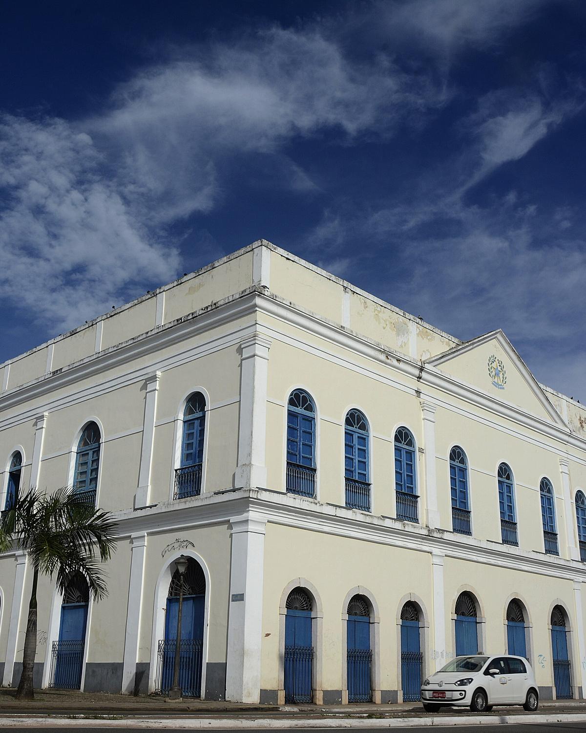Casarão amarelo claro da Casa do Maranhão visto da esquina, com janelas azuis em arco, palmeiras ao lado e céu azul