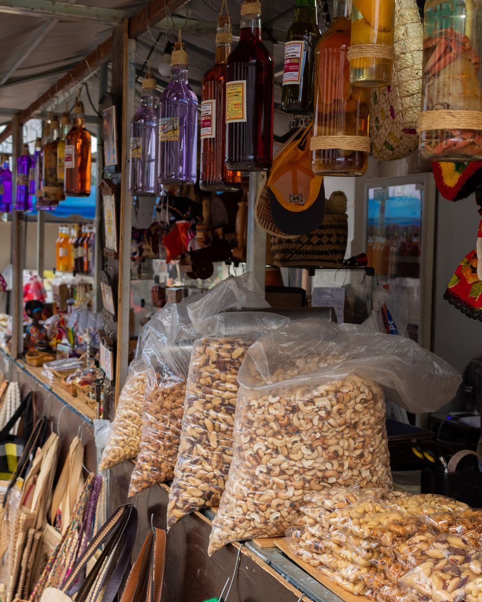 Banca de feira no centro histórico de São Luís com sacos de castanha de caju, garrafas de licor coloridas, chapéus e bolsas de artesanato pendurados na barraca