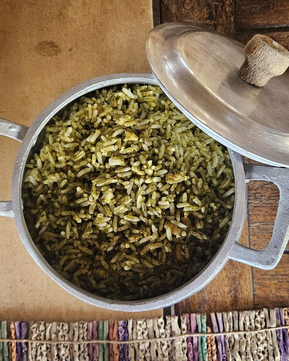 Panela de arroz de cuxá aberta sobre uma mesa de madeira, ao lado de pratos brancos e de uma esteira colorida