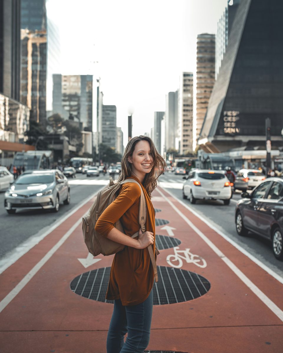 Jovem de mochila sorrindo para a câmera na ciclovia da Avenida Paulista, em São Paulo.