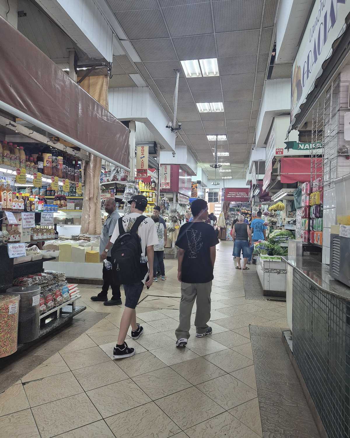 Pessoas caminhando pelo corredor do Mercado Municipal de Sorocaba, entre bancas de grãos, temperos e conservas.