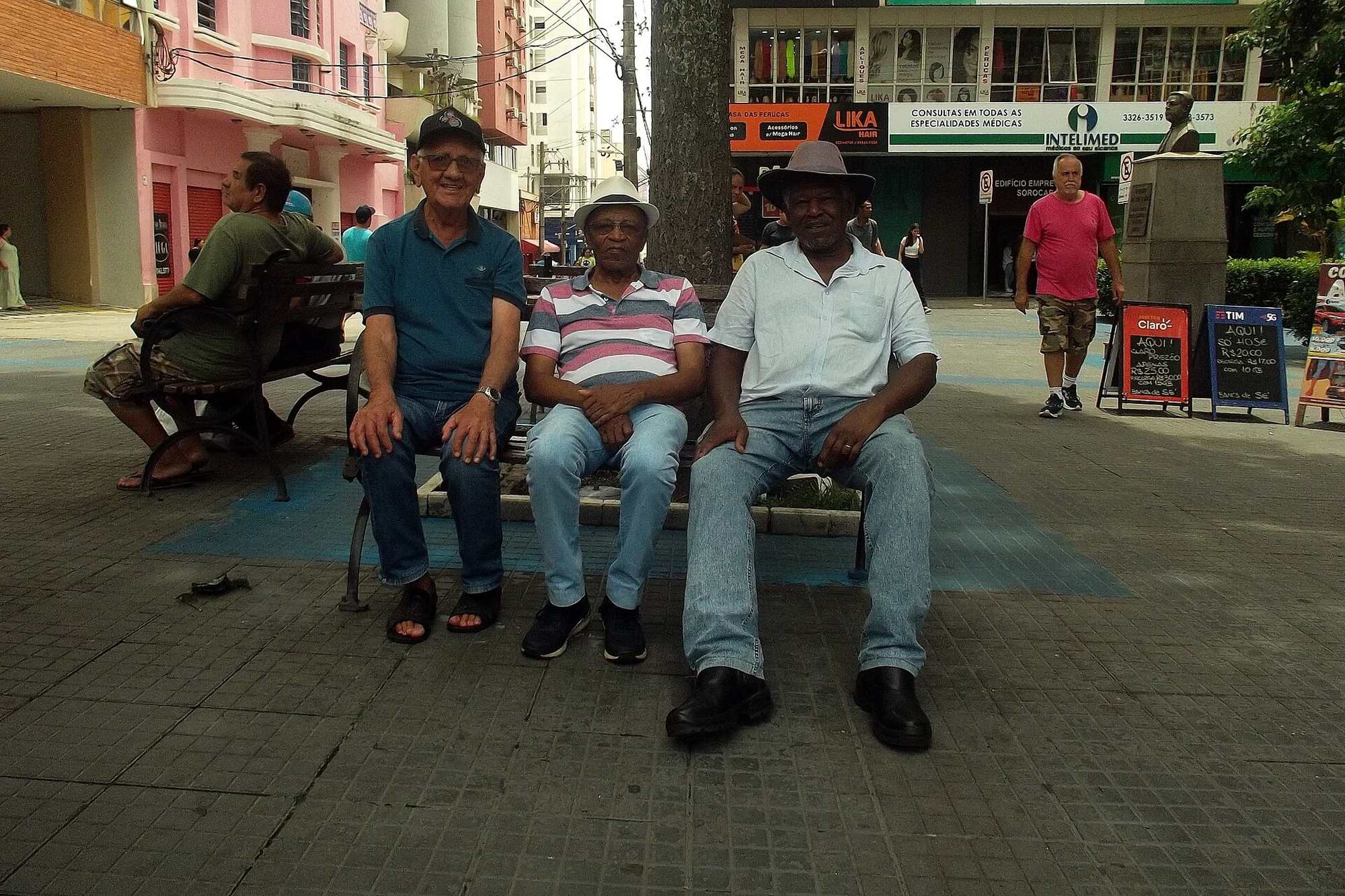 Três homens sentados num banco da praça da Catedral, no centro de Sorocaba.