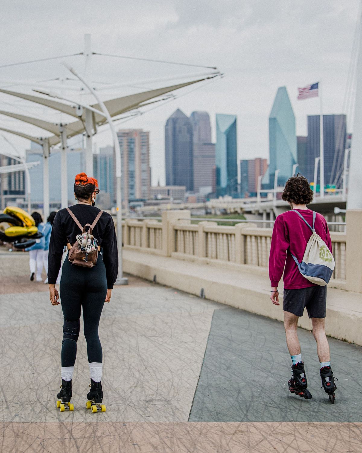 Duas pessoas de patins numa ponte de pedestres sobre o Trinity River, com os prédios do centro de Dallas ao fundo.